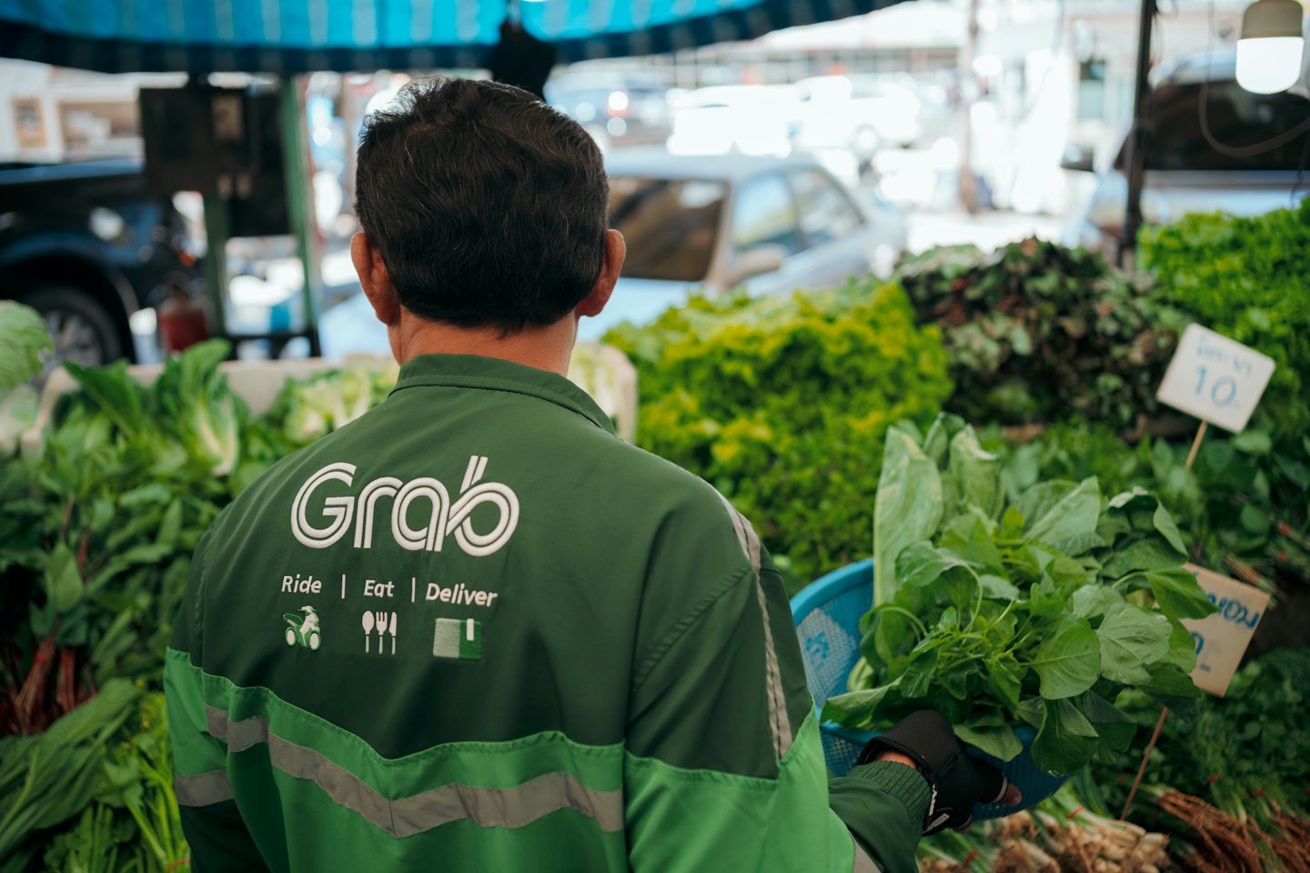 Delivery driver in green uniform picks fresh produce from a market stall.