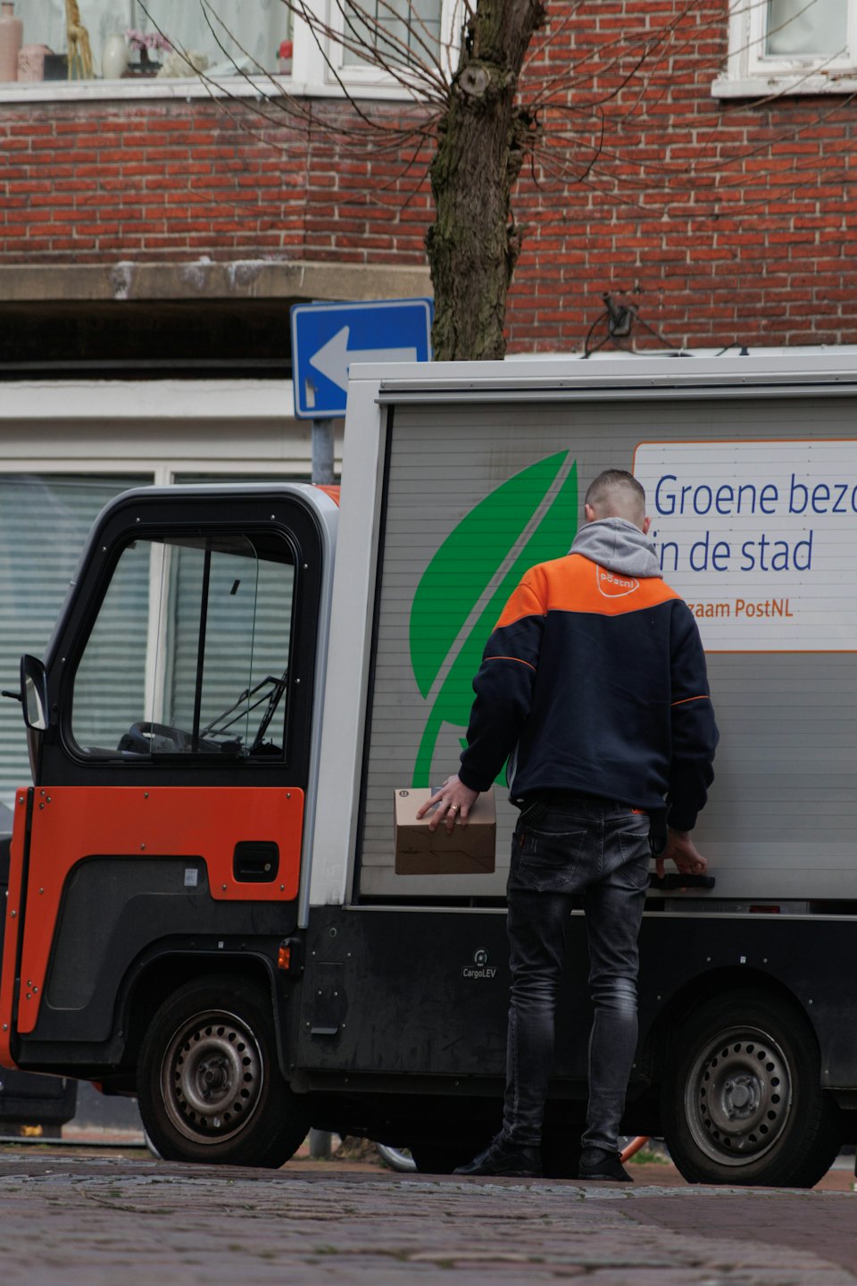Delivery person holds package next to electric vehicle on street.